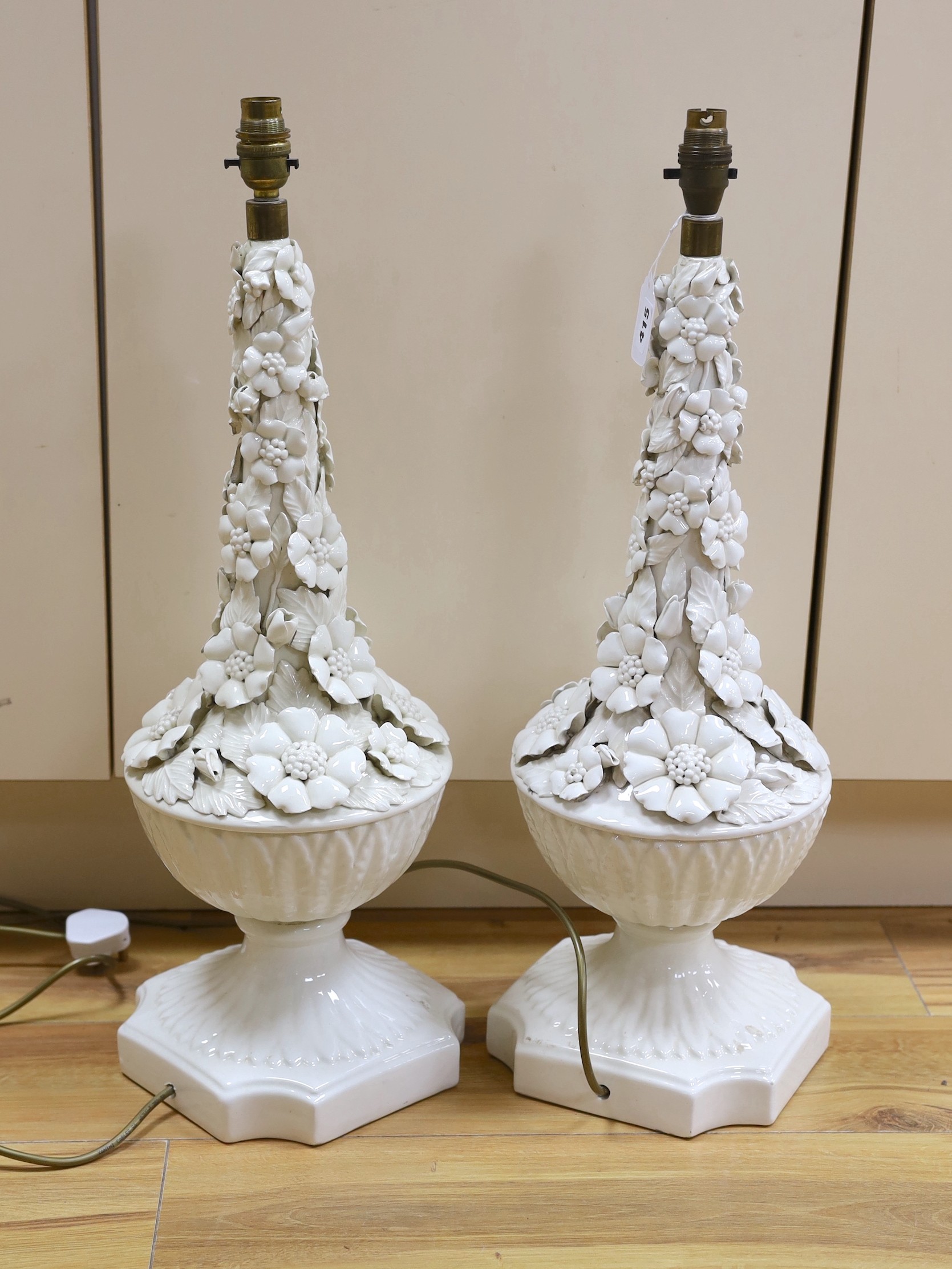 A pair of white glazed floral encrusted lamps, 58cms high not including light fitting